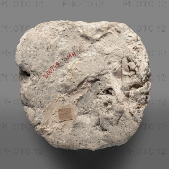Mummy mask, Round face modeled in stucco with large eyes, a wide nose, a mouth in a slight half-smile, no ears. Face height: 12 cm. Sarcophagus mask, height 12 cm, width 11.7 cm, weight 0.342 kg. 2nd century, Roman period, Egypt. Materials: stucco. Function: grave good; Egyptian art, masks, faces., A roughly circular, irregularly shaped pale object with a rough, textured surface showing areas of coarse and smoother plaster-like material; the surface has a variety of depressions, ridges, and small cavities and appears worn and crumbly in places; a small square patch of a slightly darker beige fabric-like material is affixed to one area; there are traces of a red pigment on the surface but no readable markings are described; the overall colors visible are shades of off-white, cream, beige, light gray, and touches of darker gray against a neutral medium-gray background.