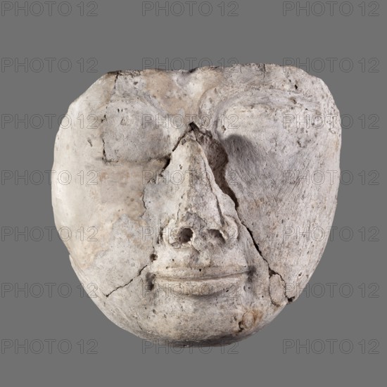 Mummy mask, round face modeled in stucco with large eyes, a wide nose, a mouth in a slight half-smile, no ears. Face height: 12 cm; sarcophagus mask, height 12 cm, width 11.7 cm, weight 0.342 kg. 2nd century, Roman period, Egypt. Masks, faces, Egyptian art, grave goods., A worn, rounded stone or plaster mask with a textured, cracked surface, showing a stylized face with pronounced eye hollows, a raised nose area with two circular nasal openings, and a subtle curved mouth; the surface has irregular fissures and pitted areas and appears to be composed of pale gray and off-white tones with patches of beige and light brown, set against a solid medium-gray background.