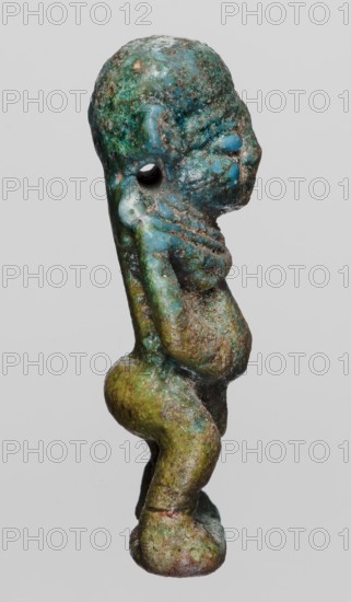 Amulet - Ptah the Dwarf Pataikos, Ptah the Dwarf myth., Egyptian deities, protective amulet, 664–332 BC; Late Period, Egypt, amulet, height 4.5 cm, width 2.2 cm, A small sculpted figure shown in profile with a textured surface displaying shades of blue, green, and brown, with remnants of darker and lighter patina; the figure has a rounded head, a pronounced forehead and nose, a visible ear and an open circular hole near the temple; the torso appears compact with rounded breasts and a slightly protruding belly, arms bent with hands placed near the head, and a narrow back that transitions into thick, bent legs and rounded feet; the surface shows rough, pitted areas and smoother glossy patches, with color variations including turquoise, teal, moss green, olive, rusty brown, and hints of pale blue against a plain light gray background.