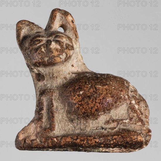 Amulet — cat; maker, inscribed or attributed to Genius, Mieczyslaw 1853–1920; subject: cat/animal; material/style: amulet; date: ca. 945–30 BC Third Intermediate Period–Ptolemaic period; place of origin: Egypt; dimensions: height 2 cm, width 2 cm., A small sculpted object shaped like a reclining animal with a rounded body and upright ears is shown against a plain light gray background; the surface of the object displays a mix of brown, reddish-brown, tan, and beige tones with speckled and worn areas, and there are smooth and rough textures visible along its body and base.