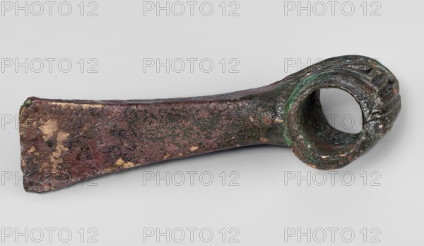 Pounder, unknown Near Eastern workshop; pounder with a low, ribbed, cylindrical socket and a blade in the form of a massive wedge set at a slight angle to the shaft. 1st half of the 2nd millennium BC; Middle Bronze Period. Western Iran find/origin. Material: metal; function: weapon. Dimensions: height 4.6 cm, width 12.5 cm, depth 3.2 cm; weight 324 g. Geometric ornaments; edged weapons; Eastern Gaulish scenography., An aged metal object with a tapered rectangular shaft leading to a rounded hollow loop; the surface shows rough, pitted texture with patches of reddish-brown, dark brown, green, and some areas of lighter tan or gold tones, and the loop end has visible striations and interior darkening.