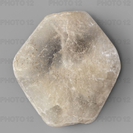 Rhomboid bead, unknown Northern Mesopotamian workshop; rhomboid bead with smooth surfaces, two corners cut off at the ends of the axis, with a drilled hole for stringing. 1st half of the 3rd millennium BC; Early Jazira III period Early Dynastic III; ca. 2600–ca. 2350 BC. Northern Mesopotamia Khabur basin; Tell Rad Shakra northeastern Syria. Found in children's graves. Height 2.2 cm; width 2.08 cm; depth 0.8 cm., A roughly hexagonal stone with rounded edges sits against a flat background; the stone shows a range of muted colors including off-white, beige, gray, and hints of brown, with areas of translucent milky white and darker gray patches, subtle speckles and streaks, and a slightly worn, uneven surface texture.