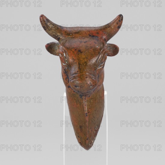 Bull-headed protoma, vessel decoration, unknown Urartian workshop. Stylized bull's head with linear details: large convex eyeballs surrounded by a straight line; two horizontal lines mark the nostrils. Small, protruding ears plastically modeled; schematically chipped horns slightly curved upward. Neck slightly elongated with a triangular bulge at the front. Rectangular cutout at the rear bottom served to mount the protoma on the rim of a cauldron. Typical Urartean cauldron decoration. 8th–7th century BC Urartu, ca. 850–585 BC. Near East; Urartu. Decoration. Weight: 134 g., A sculpted animal head with horns displayed against a plain light gray background, showing a patina of brown and reddish-brown with darker spots and hints of greenish corrosion, smooth rounded horns curving upward, small rounded ears at the sides, carved facial features with closed eyes and a pronounced snout, and a tapered elongated lower portion mounted on a clear vertical support.