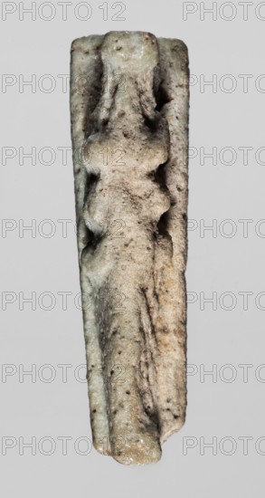 Amulet — crocodile; reclining crocodile with tail bent at the end, head slightly raised; hanging hole underneath; figurine placed on a flat rectangular base. 664–332 BC, Late Period, Egypt. Amulet; height 1.2 cm, width 3.1 cm, depth 0.8 cm., A narrow vertical object with an irregular, rough surface and an elongated shape, showing a worn, carved relief that suggests overlapping rounded forms; the surface displays a mix of pale gray, beige, light green, and muted brown tones with small dark speckles and patches of slightly darker discoloration; the background is a uniform light gray.