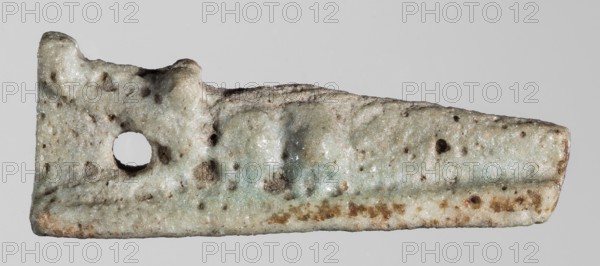 Amulet — reclining crocodile with tail bent at the end, head slightly raised; hanging hole underneath; figurine on a flat rectangular base. Protective amulet representing a sacred animal. 664–332 BC, Late Period, Egypt. Material: not specified. Dimensions: height 1.2 cm, width 3.1 cm, depth 0.8 cm., An irregular, flat object with a rough, pitted surface and an irregular rectangular shape, featuring a round hole near one end and a raised ridge running along part of its length; the surface shows a mixture of pale off-white, light gray, and muted green tones with scattered brown and rusty brown spots and speckles, and areas of subtle sheen against a plain light gray background.