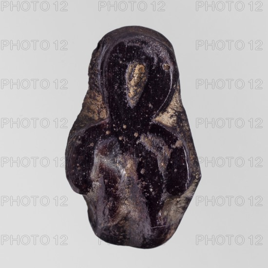 Amulet - tit;, protective amulet in the form of a tit knot with hieroglyphs; Ptolemaic Period, 332–30 BC, Egypt; amulet; height 2.2 cm, width 1.3 cm, A small carved object with an abstract rounded shape sits against a pale gray background; the object appears dark purple to near-black with areas of lighter tan and beige on raised surfaces and edges, and a few small pale speckles dot its surface, showing a glossy, slightly uneven texture and smooth carved contours suggesting rounded head and shoulder-like forms.
