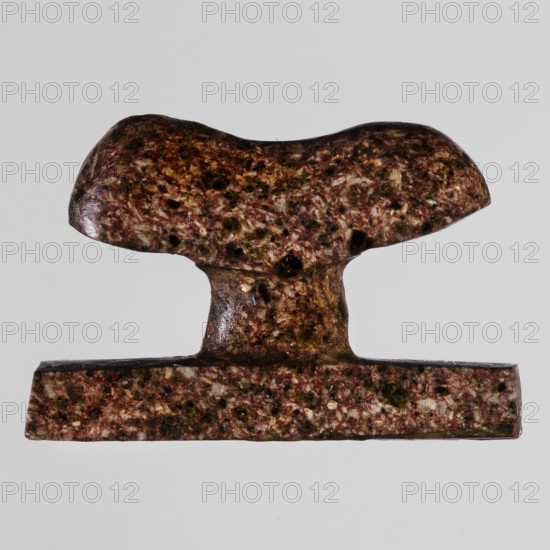 Amulet - headboard, furniture protective amulet in the shape of a miniature headboard. 664–332 BC; Late Period, Egypt. Amulet. Height 2.8 cm; width 1.8 cm., An object with a speckled surface in shades of brown, reddish-brown, dark green, and off-white, shaped with a rounded top that tapers into a short central stem and rests on a flat rectangular base; the surface shows a mottled, grainy texture with darker spots and small irregular lighter flecks against a light gray background.