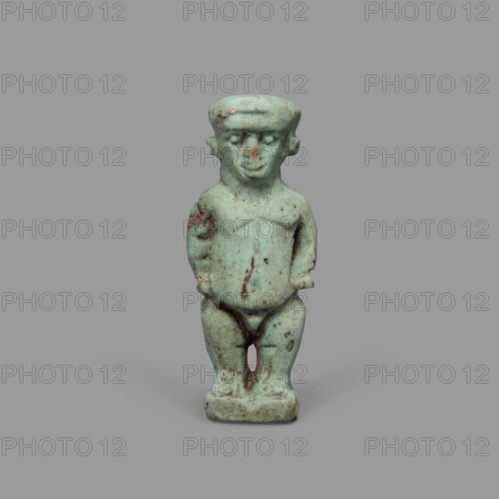 Amulet - Ptah the Dwarf Pataikos, Ptah the Dwarf myth., Egyptian deities, Egyptian religion, amulets. Amulet depicting Ptah the Dwarf Pataikos as a naked, dwarfish man standing with legs slightly apart, hands placed on his sides; figure on a rectangular base with a hole for hanging behind the neck. 664–332 BC, Late Period, Egypt. Amulet; height 4.3 cm, width 1.7 cm., A small turquoise-green figurine of a standing human-like figure with a rounded head and short hair-like band, small ears, simplified facial features, and a slightly protruding belly, with arms held close to the sides and legs together ending on a rectangular base; the surface shows several brownish spots and darker green weathering, set against a plain neutral gray background.