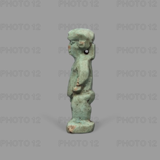 Amulet - Ptah the Dwarf Pataikos, Ptah the Dwarf myth., Egyptian deities, Egyptian religion, amulet depicting Ptah the Dwarf Pataikos as a naked, dwarfish man standing with his legs slightly apart, hands on his sides; figure on a rectangular base with a hole for hanging behind the neck. 664–332 BC, Late Period, Egypt. Amulet; height 4.3 cm, width 1.7 cm., A small standing figurine shown in profile against a plain gray background, rendered in a pale turquoise-green color with patches of brownish discoloration and wear; the figure has a rounded head with simplified facial features, a short neck with a small perforation near the ear area, a compact torso with subtly indicated arms held close to the body, and short legs standing on a rounded base, with an overall matte, slightly mottled surface texture.