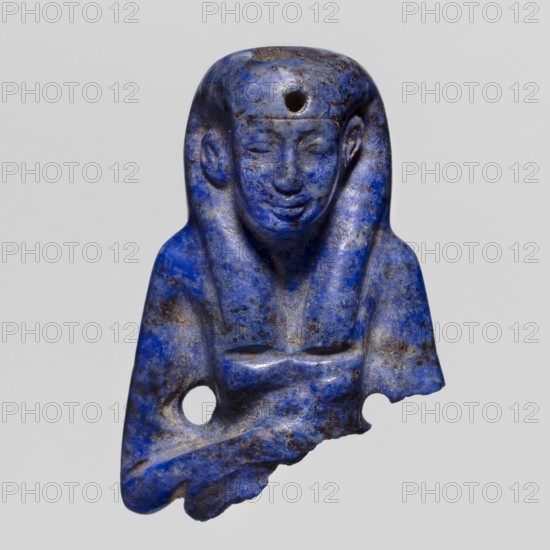 Fragment of an Isis figurine, votive figurine/amulet of the Egyptian goddess Isis, New Kingdom, ca. 1550–1069 BC, figurine, height 3 cm, width 2 cm, A carved blue stone figurine fragment depicting a human bust with a headdress, showing a face with closed eyes and a slight smile, a rounded forehead with a drilled hole, a pair of curved elements framing the face, a torso with crossed arms, irregular broken edges, and surface spots of darker and lighter blue along with areas of brownish discoloration and grey.