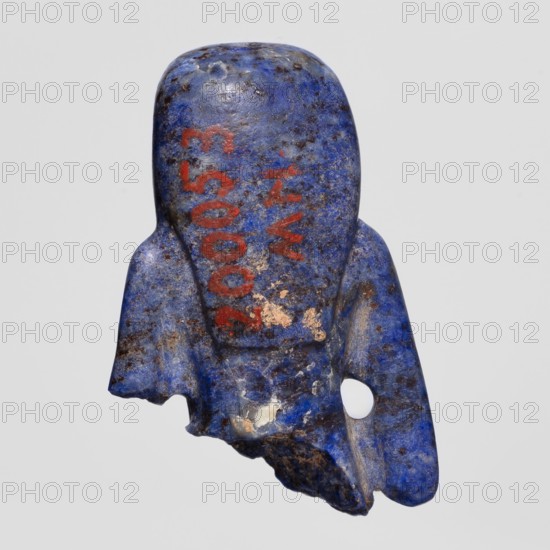 Fragment of an Isis figurine, Isis mythology, Egyptian deity; votive figurine/amulet, New Kingdom, ca. 1550–1069 BC, Egypt; height 3 cm, width 2 cm, A worn, irregularly shaped object in shades of deep blue and lighter blue with mottled dark brown or black speckling, showing areas of lighter beige or off-white where the surface is chipped; the object has a curved top and flared sides with a jagged lower edge and a rounded protrusion on one side that contains a circular hole; there are a few patches of reddish-orange pigment on the surface; the background is a pale neutral gray.