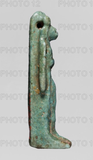 Amulet — figurine of a lion-headed goddess; lionesses; Egyptian deities; Sekhmet, Wadjit, Bastet ; lion-headed goddess with a lotus scepter in her left hand right lowered; 664–332 BC, Late Period, Egypt; amulet; height 4 cm, width 1 cm, depth 1.2 cm., A slender vertical figurine viewed in profile against a pale gray background, showing a stylized human-like form with an elongated head and a rounded back, made of a weathered turquoise-green material with areas of darker green and brownish patina; a hole is visible near the top of the head, a long raised ridge runs down the back, and a slightly projecting chest and stomach are visible along the front; there are a few small spots of reddish discoloration and traces of lighter wear on edges, with subtle variations in texture and mottling across the surface.