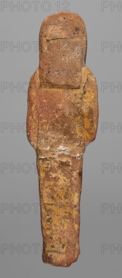 Ushabti, Restitution. Hieroglyphs; funerary figurine; mummy-shaped shabti; c. 1295–1186 BC, New Kingdom, 19th Dynasty, Egypt. Height 15.1 cm, width 4.2 cm. Arms crossed on the chest, right over left; hoes in each hand. Rectangular basket slung over both shoulders on the back. Painted tools. Wide painted usekh necklace on the chest; bracelets on the wrists. Long three-part wig, ears uncovered. Round face with large eyes, wide nose, mouth barely visible; wig and facial details painted. Painted inscription around the legs, mostly erased and illegible., A roughly human-shaped vertical object with a rounded top and a narrower lower portion, showing an overall textured, weathered surface in shades of brown, reddish-brown, yellow, ochre, and small touches of white and dark gray; the upper section is broader with subtle shoulder-like protrusions and a small rectangular patch of a lighter woven texture; the surface displays irregular mottling, flaking, and streaks of yellow pigment, with areas ...