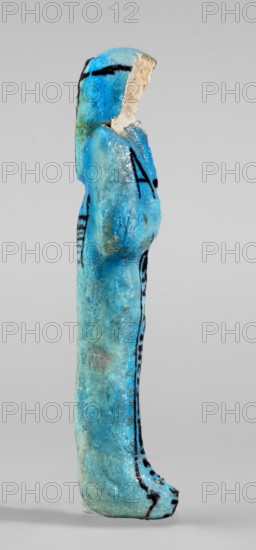 Amenhotep's shabti with baskets on the back. Arms crossed on the chest, the right folded over the left, holding hoes in both hands. Rectangular basket with loops on the back; painted tools. Wearing a three-part long smooth wig with a headband; ears covered; face damaged; painted headband. Painted inscription in one column on the front of the legs: Osiris the father of God ... scribe of the temple of Amun-Re, Amenhotep. Ca. 1069–715 BC; Third Intermediate Period, 21st–23rd Dynasty, Egypt. Shabti; height 13.3 cm, width 4.2 cm., A slender vertical figurine shaped like a standing human form, shown in profile, with a rounded head and elongated body and legs; the surface is predominantly bright turquoise blue with areas of lighter and darker blue, and several thin black painted lines and marks along the sides and head; a fractured pale beige area is visible at the face region where material is missing; the texture appears slightly rough and pitted with small speckles and spots of darker disc...