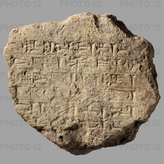 Fragment of a brick with a cuneiform inscription, Nebuchadnezzar II reign 604–562 BC, impressed with a stamp, bearing 7 lines of cuneiform commemorative text of the Babylonian king Nebuchadnezzar II Neo-Babylonian period. From Esagila Babylon / Ezida Babylon; possibly found at Borsippa, Iraq. Architectural brick, Near Eastern architecture; cuneiform writing. Material: brick with layer of bitumen. Weight: 1.6 kg. Dimensions: length max 17 cm; width 15.5 cm; thickness 7 cm brick only, 8 cm with bitumen., A roughly circular flat stone tablet with irregular edges resting against a neutral gray background, showing a textured surface of sandy beige and light brown tones with deeper brown shadows in indented areas; the tablet's face is covered with an overall grid-like pattern of shallow incisions and carved grooves creating repeated geometric impressions, with some areas appearing more worn and smoother, and a few small pits and rougher, jagged edges around the perimeter.