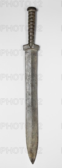 Double-edged sword, Bosporan workshop. Scen.Gal.Class., militaria, melee weapons, Black Sea region. Short sword, cast in one piece. Double-edged blade with a centric point. A slight protrusion, called the axis, runs through the center of both flats. The handle is divided into three parts: a the blade in the form of a small, slightly flattened mushroom cap b the handle shaft has a round cross-section, narrowing towards the blade, formed from 9 rings separated by grooves c the guard in the form of oblique, short leaves protruding slightly beyond the width of the blade and separated by a triangular bulge. Sword of the Cimmerian type, 6th century BC, Black Sea region, weapon. Height 55.5 cm, width 5.8 cm, depth 3.5 cm, weight 0.888 kg, length 55.3 cm, A long metallic dagger with a straight, slightly tapered blade and a rounded tip lies vertically against a pale background; the blade shows a weathered, mottled surface in shades of gray, muted green, and dull brown with visible pitting and i...