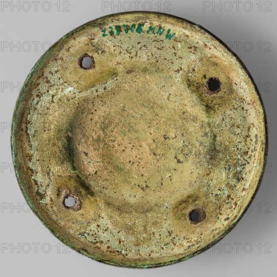 Shield boss, Bosporan workshop; round shield boss with a regularly convex central part, surrounded by a narrow plane decorated with an incised meander ornament and with four round holes arranged symmetrically; another narrow plane undecorated and diagonal, flowing into a low vertical edge; militari?/edged weapons/shields; 6th–5th century BC; Black Sea areas place of origin, weight 0.166 kg., A round, shallow metal object viewed from above with a weathered, pitted surface showing a mix of green, pale green, tan, brown, and hints of blue; the rim is slightly raised and shows darker green along the edge; there are a few irregular areas of crusty corrosion and flaking where tan and pale green meet; several small, roughly circular holes are set near the perimeter with darker brown interiors and surrounding darker discoloration; the center is slightly depressed and smoother in texture with mottled tan and green speckling.