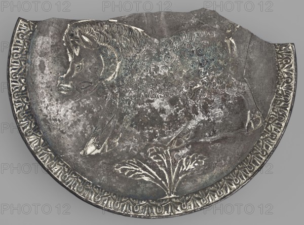 Platter with a depiction of a boar, Byzantine workshop, boar iconography, platter, 2nd half of the 5th century AD, found in Toulouse, Roman Empire 27 BC–476, vessel, weight 505.81 g, A close-up of a round metal object with a scalloped top edge showing an engraved animal in profile, appearing to have a textured, curly coat and a head with pointed ears and a snout; the animal is positioned above a stylized plant motif with broad leaves. The metal surface shows areas of wear and patina with mottled patches and subtle bluish-green and white highlights against a predominantly gray and dark silver background. A decorative band runs along the curved edge with repeating ornamental shapes in lighter silver tones contrasting with darker recesses. The overall color palette includes gray, dark silver, light silver, bluish-green, and white.