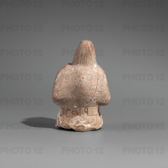 Hunchback puppet, Figurine hollow inside. Hunchbacked torso with a large head in a pointed cap set on a short neck. Elongated face with a large hooked nose and a large full-lipped mouth. Large bulging eyes with traces of white paint on the pupils. Torso wrapped in a cloak forming a thick fold around the neck and covering the right arm raised toward the chin. Left arm bent, resting at the waist. Opening on the side under the elbows for attaching legs. Opening at top of cap for attaching strings. Traces of polychrome with white paint on the torso. 1st century BC, Hellenistic period. Found at Myrmekion; origin Pantikapaion. Terracotta figurine, height 8.6 cm, width 5.5 cm, depth 4.6 cm., A small weathered clay figurine photographed from the back sits on a smooth surface against a plain background; the figurine has a rounded, tapered head and broad shoulders with a short, flared base, showing a rough, pitted texture and visible cracks and chips. The colors visible are gray, brown, tan, and...