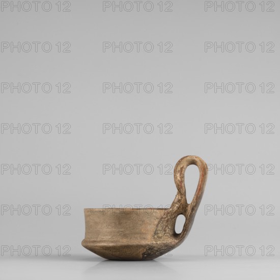 A miniature kyatos with a flat bottom and a bowl whose walls widen diagonally almost halfway up and then become vertical. At the break in the walls a sharp protrusion remains on the outer side the diameter of the upper part is smaller than the lower. The vertical handle is strongly extended upwards, attached to a protrusion on the body and to the spout, with a crossbar above the spout's edge. On the outer side the handle has a ribbon shape, then from the top widens inward with an undercut above the spout. The undercut is decorated with engraved vertical lines. Engraved lines are also incised on the bottom arranged in a grid and under the base of the handle in the shape of the letter X. The upper surface of the rim on the body is decorated with diagonal engravings, the lower part of the vertical walls with recessed dots; both rows are separated by a horizontal engraved line. Early 7th century BC, Caere; vessel; height 6.3 cm, width 7.7 cm., A small, shallow clay cup with an integrated l...