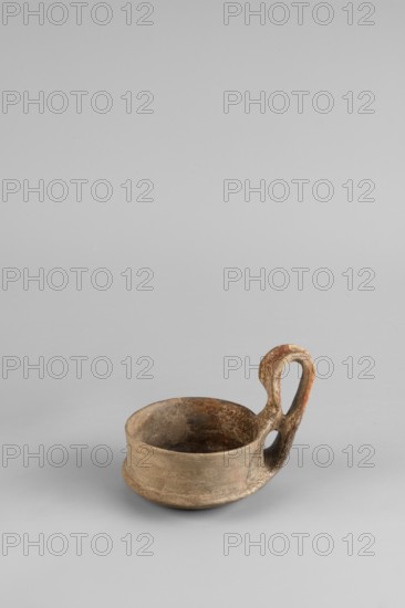 Miniature kyatos, A miniature kyatos with a flat bottom and a bowl whose walls widen diagonally almost halfway up then become vertical. Where the walls break, a sharp protrusion is left on the outer side the diameter of the upper part is smaller than the lower. The vertical handle vise is strongly extended upwards, attached to a protrusion on the body and to the spout, with a crossbar above the spout's edge. On the outer side it has a ribbon shape, then from the top widens inward with an undercut above the spout. The undercut is decorated with engraved vertical lines. Engraved lines are also on the bottom arranged in a grid and under the base of the handle in the shape of the letter X. The upper surface of the edge on the body is decorated with diagonal engravings; the lower part of the vertical walls with recessed dots. Both rows are separated by a horizontal engraved line. Early 7th century BC, Caere. Vessel, height 6.3 cm, width 7.7 cm., A small shallow bowl-like vessel with a loope...