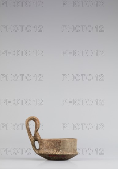 Miniature kyatos, A miniature kyatos with a flat bottom and a bowl whose walls widen diagonally almost halfway up and then become vertical. Where the walls break, a sharp protrusion remains on the outer side the diameter of the upper part is smaller than the lower. The vertical handle is strongly extended upwards, attached to a protrusion on the body and to the spout, with a crossbar above the spout's edge. On the outer side it has a ribbon shape, then from the top widens inward with an undercut above the spout. The undercut part is decorated with engraved vertical lines. Engraved lines are also found on the bottom arranged in a grid and under the base of the handle in the shape of the letter X. The upper surface of the edge on the body is decorated with diagonal engravings, the lower part of the vertical walls with recessed dots; both rows are separated by a horizontal engraved line. Early 7th century BC, Caere, vessel; height 6.3 cm, width 7.7 cm., A small ceramic vessel with an atta...