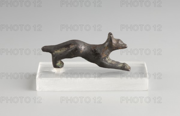 Mirror decoration, unknown author, 1st half of the 5th century BC, Corinth, mirror, height 1.8 cm, width 3.6 cm, A small dark metallic sculpture of an animal in a leaping pose rests on a translucent rectangular base; the sculpture shows a rough, patinated surface with areas of greenish and brownish discoloration and lighter spots, and the base appears white to clear with a smooth finish against a light gray background.