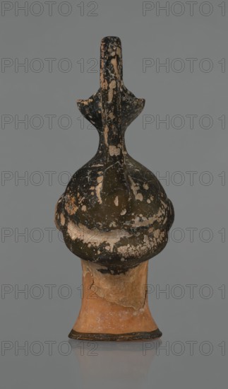 Oinochoe in the shape of a woman's head, repossession Bytom, Greece, oinochoe, head iconography, Greek culture, ancient vessels, yellowish clay, orange surface, in places shiny black engobe. Some elements painted white. Oinochoe in the shape of a woman's head. The upper part is covered with black engobe, as is the headdress, on which a white olive wreath stands out. The neck is outlined at the base with a black band. The elongated female face, very carefully modeled, corresponds to the classic Attic head type from the second half of the 5th century. The oval eyes are surrounded by a black outline. The hair is divided into two parts by a parting and falls in waves to ear level. The headdress flows into a narrow neck ending in a wide, cup-shaped spout. A cylindrical vice is attached vertically between the rim and the back of the head. Preservation condition: missing engobe in some places, damaged surface. Ca. 450 BC, Attica, oinochoe, vessel, An upright ceramic object with a rounded, bul...
