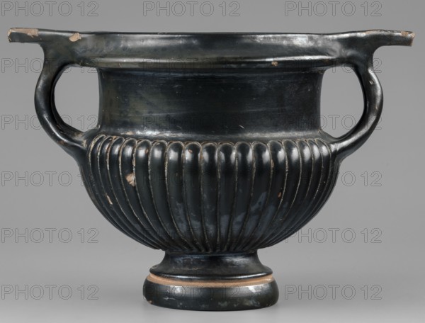 Kantharos, unknown Attic workshop, 320–310 BC. Kantharos vessel, weight 0.692 kg. The vessel has a high, echinus-shaped foot modelled with a single recess at 3/4 of its height. Rounded, fluted body under the vises the recesses take an oblique direction creating a three-leaf pattern — on one side the side vises are ajar due to lack of space, narrow shoulders, and a high, smooth neck. The vises are strongly rounded. Modelled spout with a strip below the rim, and characteristic horizontal, elongated, triangular, slightly raised handles above the vises. The bottom features an ornament of six 13-leaf palmettes, not entirely symmetrically arranged; above them a roulette-like decoration 6 rows. The entire vessel, including the inner surface of the foot, is covered with varnish except for the edge of the foot on which the vessel stands and a single depression on the foot. Technology: Shiny, rather metallic varnish distributed evenly over the surface. Preservation: A few chips, abrasions, and s...