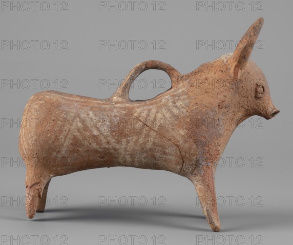 Bull-shaped vessel, Vessel in the shape of a bull standing on widely spaced legs. Cylindrical body with straight cut flowing into a wide neck. Small head with cylindrical muzzle, plastically crafted eyes and horns protruding upwards. Hole in the neck; beneath it a spout askos form, the other end attached in the middle of the back. Surface covered with geometrically painted decoration. Cypriot pottery, 1300–1200 BC. Vessel askos; height 11 cm, width 13 cm, depth 4.5 cm, weight 0.11 kg., A small sculpted animal form with a rounded body and elongated snout stands on a few stubby legs, showing a textured surface of worn terracotta tones including shades of brown, reddish-brown, and pale beige; the piece has a curved handle on its back, a raised ear, a circular raised feature where an eye would be, and visible surface irregularities and cracks against a neutral gray background.