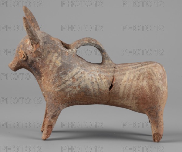 Bull-shaped vessel. Vessel in the shape of a bull standing on widely spaced legs. The cylindrical body, straight cut, flows into a wide neck. The head is small with a cylindrical muzzle, with plastically crafted eyes and horns protruding upwards. There is a hole in the neck, and beneath it is a spout, the other end of which is attached in the middle of the back. The surface is covered with geometrically painted decoration. Cypriot pottery, askos. 1300–1200 BC, Cyprus. Height 11 cm, width 13 cm, depth 4.5 cm, weight 0.11 kg. Bulls; animal figurines., A weathered animal-shaped ceramic vessel with a rounded body, four slender legs, a pronounced snout, upright pointed ears, and a looped handle on its back; the surface shows worn painted patterns and areas of flaking and cracks. Visible colors include shades of brown, tan, beige, rust, gray, and small patches of off-white.