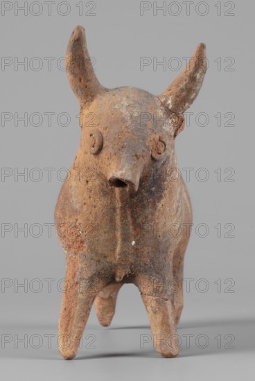 Bull-shaped vessel, Bull-shaped vessel in the shape of a bull standing on widely spaced legs. The cylindrical body, straight cut, flows into a wide neck. The head is small with a cylindrical muzzle, with plastically crafted eyes and horns protruding upwards. There is a hole in the neck, and beneath it is a handle, the other end of which is attached in the middle of the back. The surface is covered with geometrically painted decoration. 1300–1200 BC, Cyprus. Vessel askos. Height 11 cm; width 13 cm; depth 4.5 cm; weight 0.11 kg., A small, weathered terracotta animal figurine with a rounded body and elongated snout stands on several slender legs against a neutral background, showing a rough, pitted surface with patches of brown, reddish-brown, tan, and gray; two upward-pointing horn-like projections extend from the top of its head, and small circular ear shapes are visible on the sides, while the overall form displays irregular texture, chips, and worn areas.