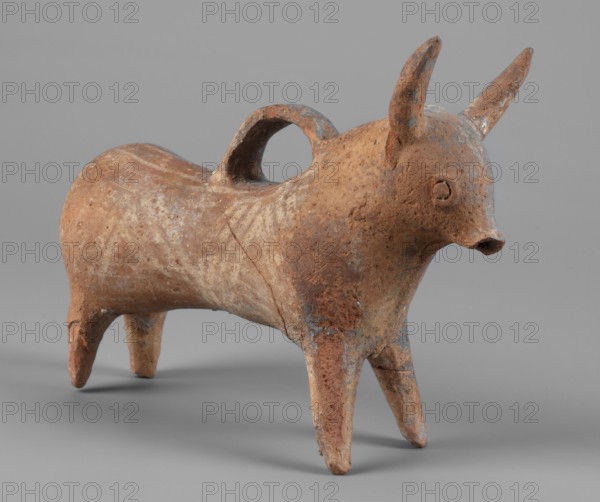 Bull-shaped vessel, Vessel in the shape of a bull standing on widely spaced legs. The cylindrical body, straight cut, flows into a wide neck. The head is small with a cylindrical muzzle, with plastically crafted eyes and horns protruding upwards. There is a hole in the neck, and beneath it is a vice, the other end of which is attached in the middle of the back. The surface is covered with geometrically painted decoration. Bulls, animal figurines, Cypriot pottery. 1300–1200 BC, Cyprus. Vessel askos. Height 11 cm, width 13 cm, depth 4.5 cm, weight 0.11 kg., A small sculpted animal figure with a rounded body and four tapered legs, showing a textured surface and weathered areas in shades of brown, rust, tan, and touches of gray; the head has two upright pointed horns and a short projecting snout, with simple circular eye details; a curved handle arches over the back from the head area to the rear; the piece rests on a smooth neutral gray background.