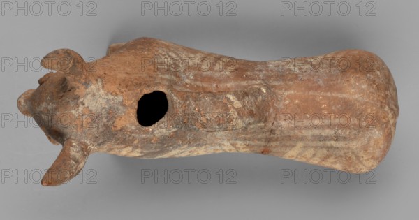 Bull-shaped vessel, Vessel in the shape of a bull standing on widely spaced legs. The cylindrical body, straight cut, flows into a wide neck. The head is small with a cylindrical muzzle, with plastically crafted eyes and horns protruding upwards. There is a hole in the neck, and beneath it is a vice, the other end of which is attached in the middle of the back. The surface is covered with geometrically painted decoration. 1300–1200 BC, Cyprus. Vessel askos. Height 11 cm, width 13 cm, depth 4.5 cm, weight 0.11 kg., A weathered, elongated clay object shaped roughly like an animal form lies against a neutral gray background, showing a textured surface with worn areas and irregular patches. The object displays a mix of earthy colors including shades of brown, reddish-brown, beige, and pale gray, with lighter streaks and mottled spots across its body. One end has two tapered protrusions resembling ears or horns and a rounded snout-like form, while the midsection features a dark irregular ho...