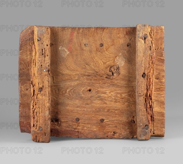 Canopic box with the falcon Sokaris on the roof;, falcons, djed pillars, tit iconography; naos; grave goods; 664–525 BC, Late Period, 26th Dynasty, Egypt; canopic box; height 42 cm, width 22.5 cm, depth 29.5 cm, weight 2.414 kg., A rectangular piece of weathered wood photographed against a gray background, showing a flat central panel with visible grain patterns and knots in shades of brown and tan, flanked by two vertical wooden slats attached with round dark metal fasteners; the slats have rough, splintered textures and irregular edges with areas of deeper reddish-brown and lighter beige where the surface is worn, while the central panel displays swirling grain in golden-brown and honey tones with small holes and darker brown spots.