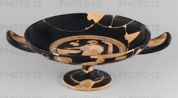 Red-figure kylix with a bathing scene, the Boots Painter ca. 460 BC. Bath iconography; Greek ceramics. Physical description: goblet with slightly parted rim edges, shallow bowl, low stem, and flat foot. Vices have a round cross-section, slightly raised tops reaching the line of the rim. Conical bottom. Sleeve-shaped foot. Scene: Women wash at lutrions bowls on high bases, pass around folded garments, and one of them ties characteristic high boots. Technique: Thick, very good quality varnish, evenly distributed; smooth surface; traces of turning invisible, brush marks visible. Mixture: mica. Condition notes: Artifact glued from many fragments with visible conservation restorations; surface contaminated; visible secondary losses and chips; standing surface heavily worn. Attributed to Kamila Nocon; provenance/attribution notes: Attica Athens, Tarquinia Beazley 1928. Kylix; vessel. Dimensions: height 9.2 cm, width 29.8 cm, depth 22.8 cm, weight 0.53 kg., A shallow, wide ceramic bowl with a...