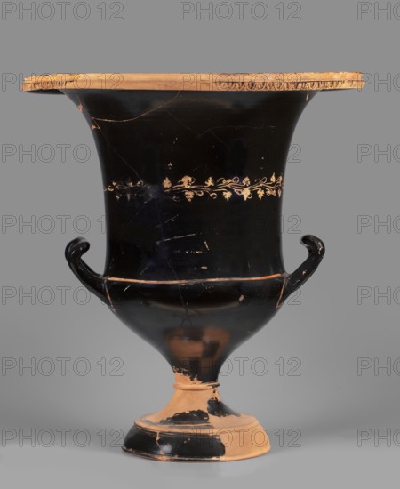 Chalice krater. Numerous gluings on the foot and the upper part of the body and rim; at the joints there are modern impressions and additions, the rim is partially filled. Varnish has been painted over in places to conceal the repairs. Black-figure krater decorated with a band around the center of the body featuring a vine leaves and clusters painted in pink and gold. Rim decorated with an egg-shaped motif showing traces of gilding. 5th century BC, Attica. Cup krater krater, vessel. Height 56.7 cm; width 36 cm with vices; foot diameter 22 cm; weight 7.3 kg., A large, tall vase with a flared rim and two curved handles sits against a gray background; the vase shows a glossy black surface with worn areas revealing a tan clay beneath, a decorative band of delicate vine-and-leaf motifs encircles the upper body in a lighter tan color, the rim edge has a series of small carved or incised semicircular patterns in tan, the handles curl outward and upward and are black with patches of wear, the ...
