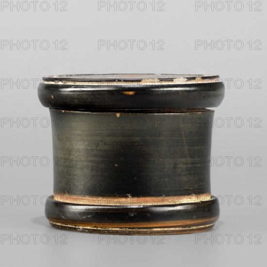 Red-figure pyxis with an image of a hand on the lid. Small pyxis with lid; cylindrical shape, separated foot, concave bottom. Flat lid with slightly protruding edges; rounded sides. Image of a hand on the lid. Technology: Glossy, high-quality varnish, evenly distributed but unevenly fired, green shades visible in places. Smooth surface; cleaned clay; traces of turning visible under the varnish. Admixtures: mica. Condition: intact; white deposit visible on the inside surface of the lid; secondary losses and abrasions visible. 5th century BC, Attica; Arsinoe findspot; Athens place of origin. Pyxis vessel. Weight 0.10 kg., A short cylindrical object with rounded top and bottom edges sits against a plain light gray background, the object showing a dark surface with worn areas revealing brown and tan underneath, and small patches of lighter beige wear; the top and bottom rims are slightly raised and glossy with a mix of black, dark brown, and hints of tan, while the central band has a more ...