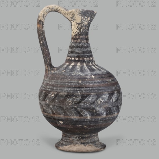 Oinochoe, unknown Cypriot workshop, Arsinoe Cyprus. Oinochoe on a cup-shaped foot with a spherical body transitioning into sloping arms, separated by a recess from the narrow, tapering neck terminating in a triangular rim. The band-shaped vise protrudes slightly above the rim and is connected to the arm. The vessel is covered with gray-blue, matte paint. Decoration in white and brown paint surrounds the vessel concentrically. On the foot, stripes of white paint decorate the body; a laurel sprig adorns the narrowest part of the body, with white and brown stripes above it. On the shoulders, a ray ornament extends up to the neck. On the neck at the base and under the rim, white dots, and between the rows of dots, white stripes. 332–30 BC; Hellenistic period, Cyprus. Oinochoe vessel, height 14 cm, width 9 cm., An aged ceramic jug with a rounded body, a narrow neck, a flared spout, and a high curved handle; the surface shows worn painted patterns including bands and leaf-like motifs, with v...