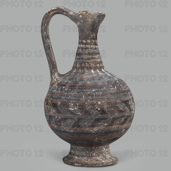 Oinochoe, unknown Cypriot workshop; Arsinoe Cyprus. Oinochoe on a cup-shaped foot with a spherical body transitioning into sloping arms, separated by a recess from the narrow, tapering neck terminating in a triangular rim. The band-shaped handle protrudes slightly above the rim and is connected to the arm. The vessel is covered with gray-blue, matte paint. Decoration in white and brown paint surrounds the vessel concentrically. On the foot, stripes of white paint decorate the body; a laurel sprig adorns the narrowest part of the body, with white and brown stripes above it. On the shoulders, a ray ornament extends up to the neck. On the neck at the base and under the rim, white dots, and between the rows of dots, white stripes. 332–30 BC; Hellenistic period, Cyprus. Oinochoe vessel, height 14 cm, width 9 cm., A round-bodied ceramic jug with a single curved handle and a narrow neck ending in a small spout stands against a plain background; the surface shows worn painted bands and pattern...
