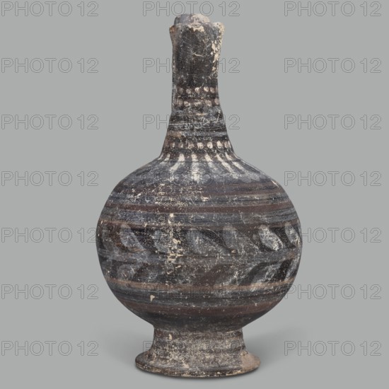 Oinochoe, unknown Cypriot workshop; Arsinoe Cyprus. Oinochoe on a cup-shaped foot with a spherical body transitioning into sloping arms, separated by a recess from the narrow, tapering neck terminating in a triangular rim. The band-shaped handle protrudes slightly above the rim and is connected to the arm. The vessel is covered with gray-blue, matte paint. Decoration in white and brown paint surrounds the vessel concentrically. On the foot, stripes of white paint decorate the body; a laurel sprig adorns the narrowest part of the body, with white and brown stripes above it. On the shoulders, a ray ornament extends up to the neck. On the neck at the base and under the rim, white dots, and between the rows of dots, white stripes. 332–30 BC; Hellenistic period, Cyprus. Oinochoe vessel, height 14 cm, width 9 cm., A rounded ceramic vessel with a narrow neck and flared foot, shown against a plain gray background. The surface of the vessel displays worn horizontal bands and decorative patterns...
