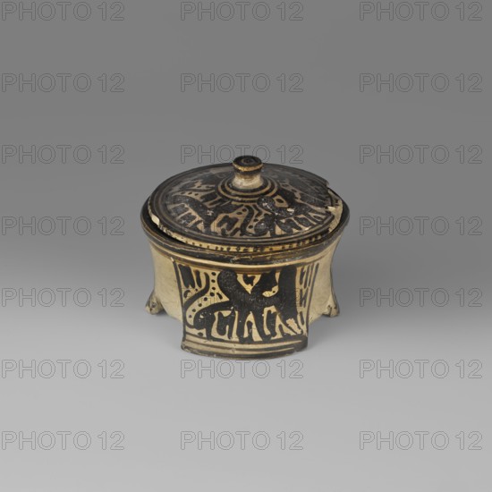 Orientalising pyxis in the Silhouette style with depictions of sphinxes and animals; attributed to Corinth; dated 590–550 BC Middle to Late Corinthian periods. Asymmetrical, thin-walled, three-legged pyxis with a lid. The walls are slightly concave and the bottom flat. Outer surface at the rim edge has a wide band of black varnish, narrower below. Decoration in three areas: two sphinxes and a panther executed in silhouette technique, with a small amount of simplified filling ornamentation. Inner surface left the color of the clay except for a ~4 mm black-painted strip beneath the rim. The lid repeats a silhouette motif from the body. Surface smooth, shiny and evenly distributed varnish; cleaned pale yellow clay with visible turning traces. Visible losses on the lid. Clay color: 2.5 Y 8/3 pale yellow. Varnish color: 2.5 Y 3/1 very dark gray. Type: Corinthian pyxis vessel. Height 7.5 cm, width 8.5 cm, weight 0.118 kg., A small round lidded ceramic container sits on a neutral gray surface...