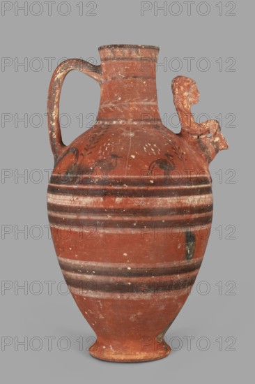 Jug with a figurine of a woman with a jug. Cypriot pottery, female figurines applique. Jug on a foot resembling an inverted echinus with a belly widening by convex shoulders, separated from a cylindrical neck with a straight spout. A two-part vise connects the neck with the shoulders, and on the side opposite the vise is the bust of a woman with a jug. Decoration executed in white and black paint: the belly at its widest point and along one-third of its height is decorated with alternating white and black concentric bands. Beneath the vise, a wavy black stripe extends onto the shoulders on both sides. On both sides, the shoulders feature two birds among plants, a row of dots and a concentric stripe at the base of the neck; a branch with leaves encircles the neck above, and black triangles on a white background at the edge. Dated 480–400 BC, Cypriot—Classical Period I; provenance: Arsinoe Marion. Vessel; height 35 cm, width 19 cm, weight 1.72 kg., An earthenware jug with a rounded body ...