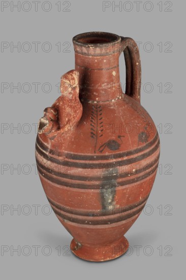 Jug with a figurine of a woman with a jug; Cypriot pottery, female appliqué figurine. Jug on a foot resembling an inverted echinus with a belly widening by convex shoulders, separated from a cylindrical neck with a straight spout. A two-part vise connects the neck with the shoulders; on the side opposite the vise is the bust of a woman holding a jug. Decoration in white and black paint: the belly at its widest point and along one-third of its height is decorated with alternating white and black concentric bands; beneath the vise a wavy black stripe extends onto the shoulders on both sides. Shoulders feature, on both sides, two birds among plants, a row of dots and a concentric stripe at the base of the neck; a branch with leaves encircles the neck above, and black triangles on a white background at the edge. 480–400 BC; Cypriot — Classical Period I. Arsinoe Marion. Vessel; height 35 cm, width 19 cm, weight 1.72 kg., A terracotta jug in reddish-brown with darker brown bands and painted ...