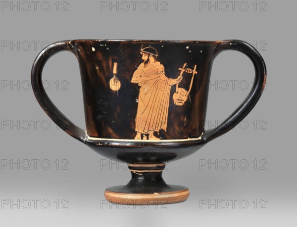 Red-figure kantharos with a depiction of an ephebe with an aryballos and a Greek inscription “Beautiful boy”., Kantharos with a slightly flared spout, a deep bowl, a flat bottom, a high profiled stem, a ring-shaped foot. Thin-walled. A obverse: bearded man with a lyre in his head in left profile, holding a lyre in his left hand. B reverse: ephebe with aryballos. The inner surface of the bowl is covered with varnish. Technology: smooth surface; varnish thick, shiny, unevenly fired. Notes: vessel intact; small secondary losses and chips visible on the surface. Varnish color: 10 YR 2/1 black. Date: ca. 450 BC mid-5th century BC. Provenance: Attica. Type: kantharos, vessel. Dimensions: height 11 cm; width 16.2 cm; depth 10.2 cm., A black ceramic two-handled cup on a short pedestal with a rounded base, decorated with an orange-figure scene showing a robed standing figure holding a stringed instrument in one hand and a rounded object nearby, with worn areas and small chips. Colors visible in...