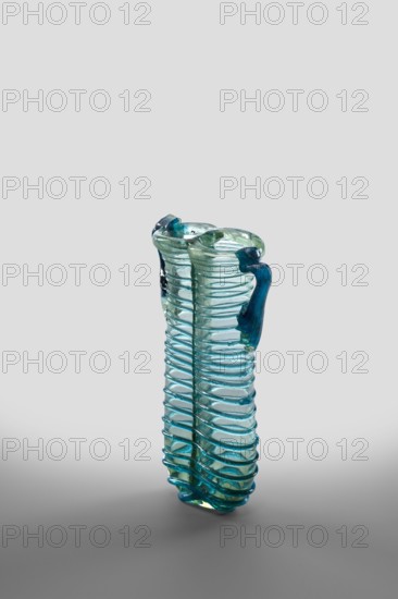 Dilekyt, unknown Syrian workshop; lekythos glass vessel, Barag type XII:2-1. Transparent colorless glass with a light bluish-green shade; decoration of a spirally twisted thread of translucent blue glass; free-blown; tube with spirally applied thread folded in half. Outer diameter of rim: 1 – 3.20 cm, 2 – 2.70 cm. 4th century. Vessel height 11.7 cm, width 7.2 cm, depth 3.2 cm, weight 0.08 kg., A tall translucent glass vase with a ribbed spiral texture and a pair of curved handles, rendered in shades of blue and green; the glass shows variations from light aqua to deeper teal, with glossy highlights and internal bubbles, standing on a smooth neutral gray surface against a pale gray background.