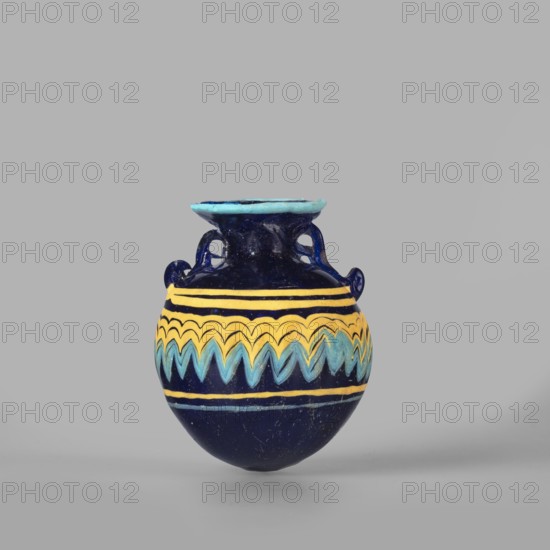 Globular aryballos, Egyptian workshop attributed, globular aryballos decorated at the widest point of the body with a vertically grooved band of zigzag decoration, changing into spirals at the bottom and top of the body. Navy blue glass; thread decoration, embedded blue and yellow. 6th–4th century BC., Aryballos vessel; weight 0.05 kg; height 6.5 cm; diameter 5.6 cm., A small rounded vase sits centered against a plain light gray background, predominantly deep blue in color with a glossy finish; the neck and rim show a lighter turquoise blue, and there are decorative bands of bright yellow and pale blue forming wavy and zigzag patterns around the body, with two small looped handles on the upper sides and a slightly flared rim.