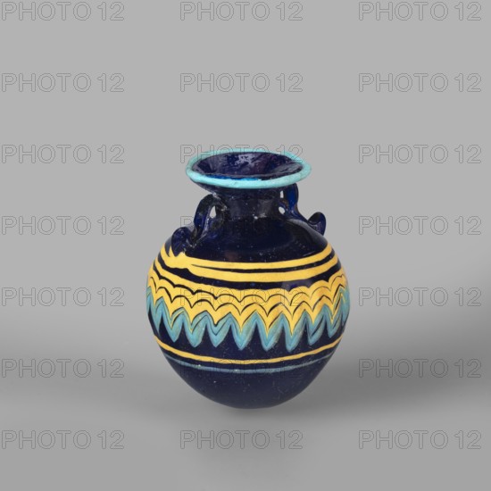 Globular aryballos, Egyptian workshop attributed, globular aryballos decorated at the widest point of the body with a vertically grooved band of zigzag decoration, changing into spirals at the bottom and top of the body. Navy blue glass; thread decoration, embedded blue and yellow; 6th–4th century BC; place of origin, aryballos vessel; weight 0.05 kg; height 6.5 cm; diameter 5.6 cm., A small rounded ceramic vessel with a flared rim and two small loop handles, predominantly deep blue in color with bands of yellow and aqua decorative zigzag and stripe patterns around its midsection; the rim has a lighter turquoise blue edge, and the background is a uniform light gray.