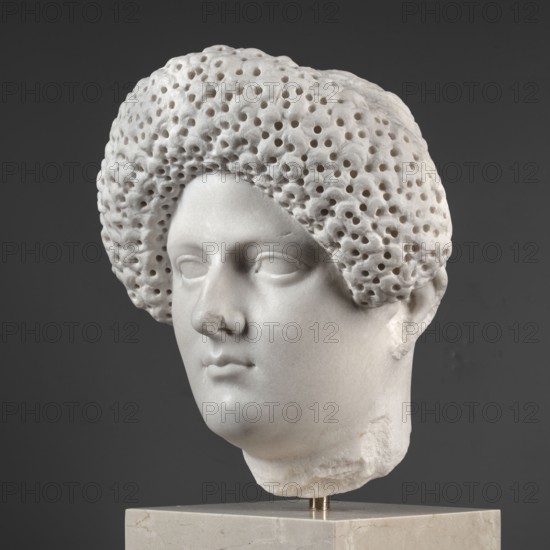 Portrait of a Roman woman, Head with a broad, round, full face and a triangular forehead; elaborate hairstyle: hair twisted into small curls marked with a gimlet, the rest gathered at the back in a small bun. Female portrait, Roman sculpture, masterpiece. Date: 82–92 CE, Rome, Roman Empire 27 BC–476. Sculpture. Height 30.5 cm, width 27 cm, depth 25 cm, weight 36.5 kg., A marble sculpted head of a person displayed on a light beige stone base against a dark gray background, showing a smooth pale white face with closed or uncarved eyes, a rounded nose, and closed lips, and a textured hair mass surrounding the head characterized by a dense pattern of round holes and an overall off-white color with subtle gray shadows.