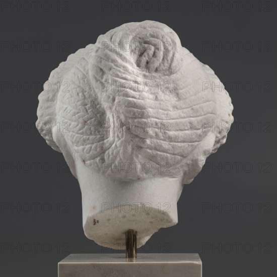 Portrait of a Roman woman, Head with a broad face and an elaborate hairstyle: hair twisted into small curls marked with a gimlet; the rest gathered at the back in a small bun. Round, full face, with a triangular forehead. Roman sculpture, female portrait, masterpiece, ca. 82–92 CE, Rome, Roman Empire 27 BC–476, sculpture. Dimensions: height 30.5 cm, width 27 cm, depth 25 cm; weight 36.5 kg., A light-colored sculpted object viewed from behind showing a textured, rounded top with layered, ribbed patterns and carved folds forming a central spiral; the lower portion tapers into a smoother neck-like base mounted on a vertical metal rod and set into a rectangular block; visible colors include shades of white, off-white, gray, dark gray, and a few small brownish spots.